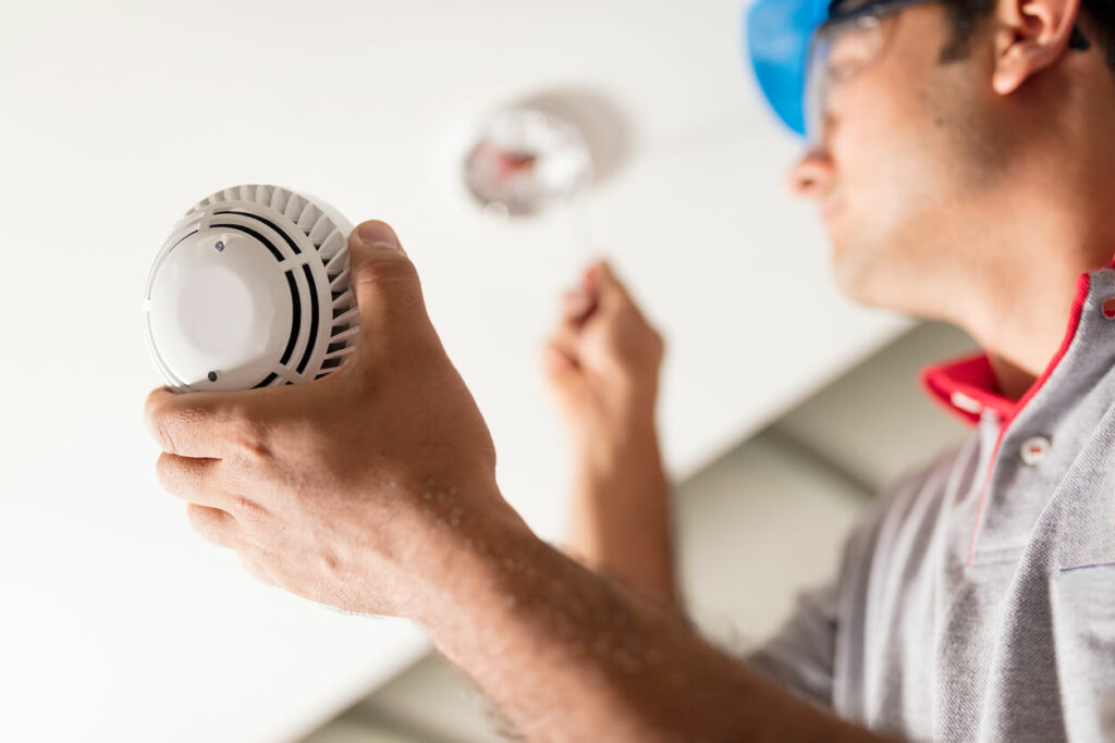 A technician wearing a hard hat and safety glasses is installing domestic fire sprinkler.